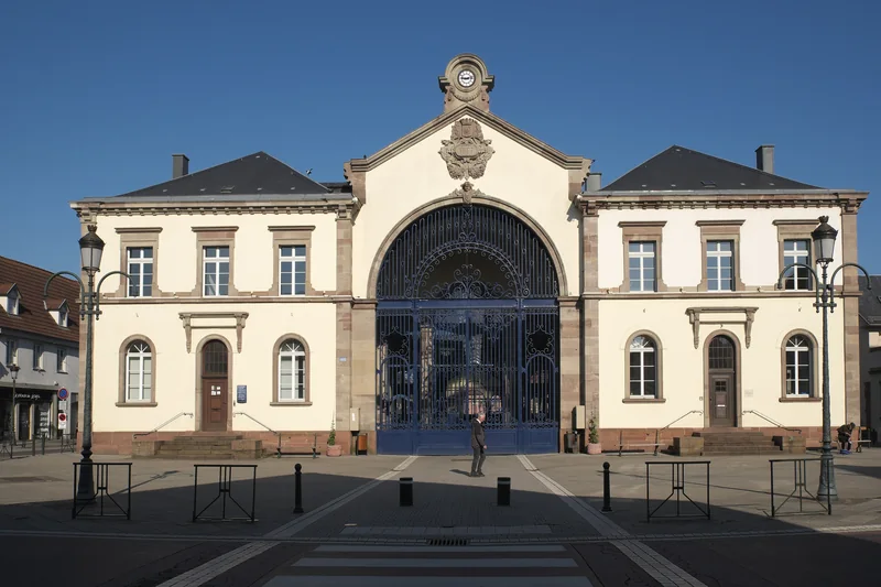 La halle aux houblons de Haguenau : bâtiment à fronton et grande porte en fer forgé, vu de face depuis la place, en 2019.