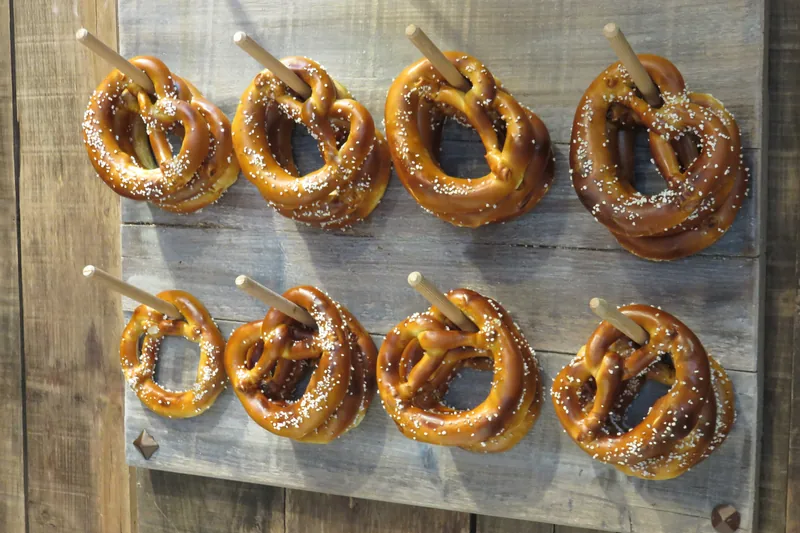 Huit bretzels alsaciens salés, piqués sur des bâtons de bois et accrochés à une planche, photographiés de face en 2015.