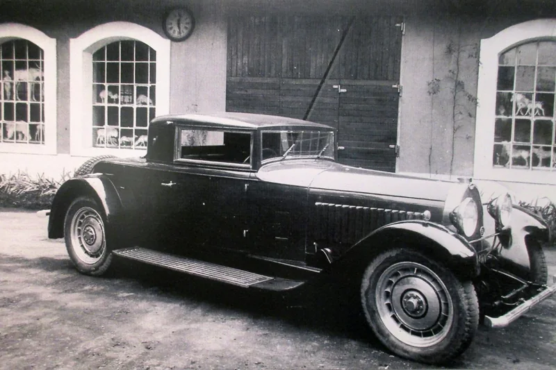 Une Bugatti Type 46 de 1931 stationnée devant les bâtiments de l'usine de Molsheim, photographie ancienne en noir et blanc.