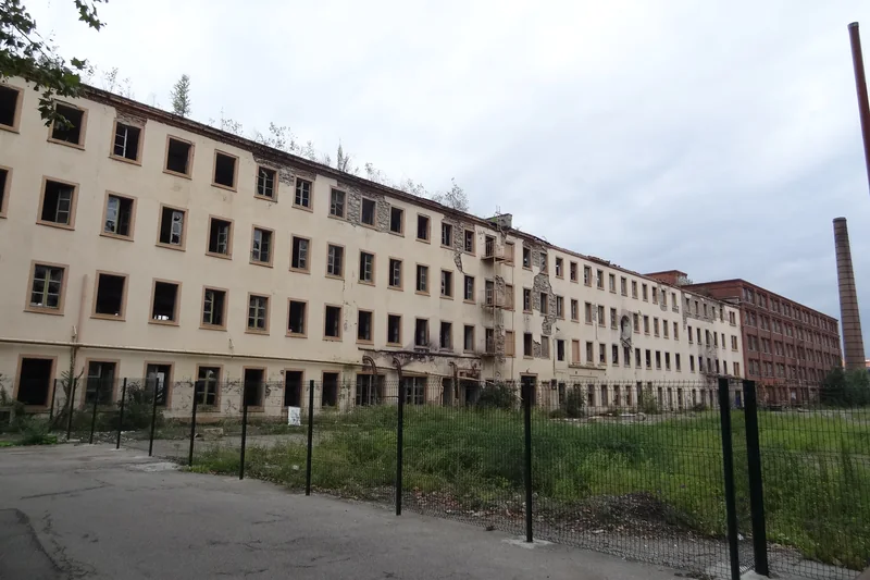 La filature géante de 1812 sur le site DMC de Mulhouse : long bâtiment à nombreuses fenêtres derrière une clôture, en 2013.