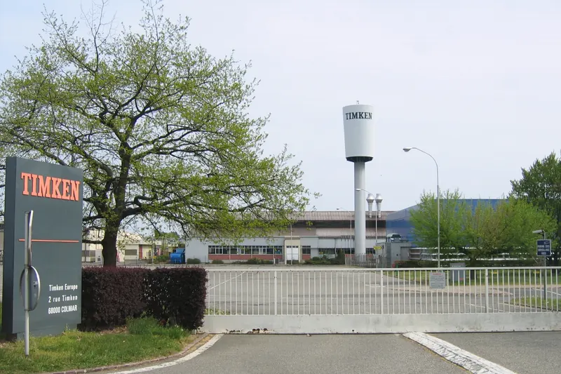 L'entrée de l'usine Timken à Colmar : panneau à l'enseigne de l'entreprise, château d'eau et halls derrière la barrière.