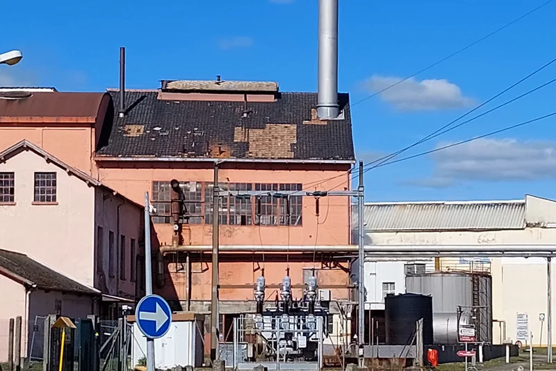 Bâtiments de l'usine de papier de Schweighouse-sur-Moder derrière une clôture, avec une cheminée et un poste électrique.