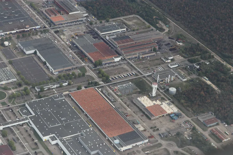 Vue aérienne oblique de l'usine Stellantis de Mulhouse : grands halls, parkings et forêt tout autour, en septembre 2026.