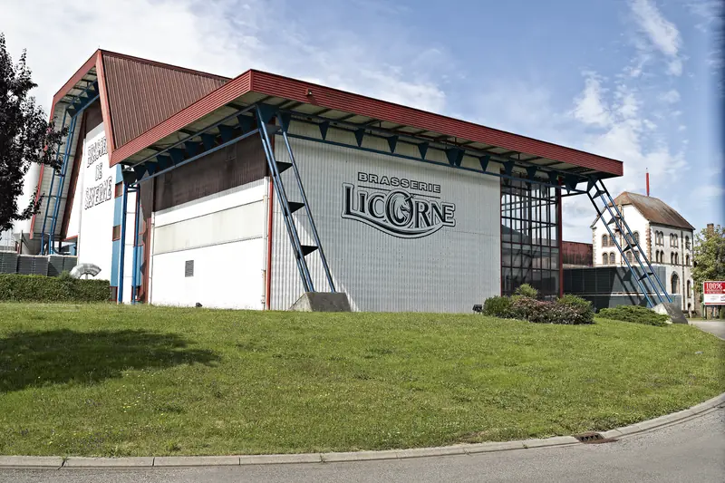 La brasserie Licorne à Saverne : grand hall gris portant le nom de la marque, et ancien bâtiment de brasserie derrière.