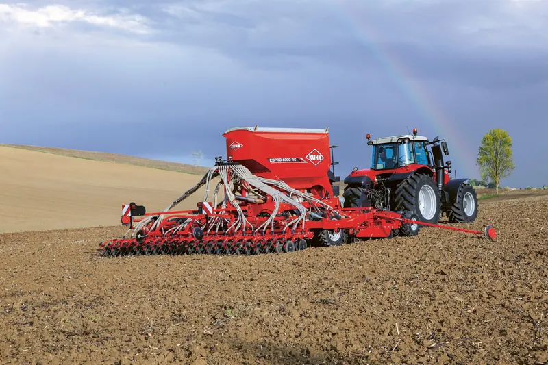 Un semoir Kuhn Espro attelé à un tracteur dans un champ labouré, sous un ciel bleu, en 2024.