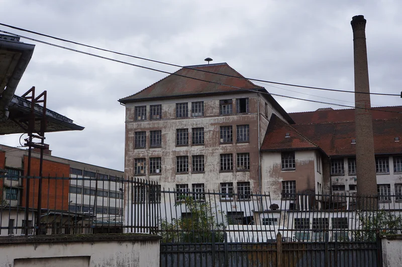 Ancien bâtiment industriel à étages et haute cheminée de brique, derrière une clôture, dans le port du Rhin à Strasbourg.