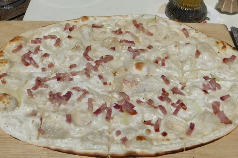 Tarte flambée alsacienne aux lardons et aux oignons, sur une planche en bois, photographiée de dessus à Strasbourg en 2012.
