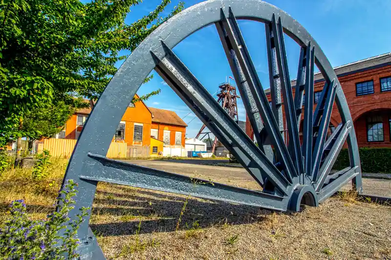 Une grande roue de molette du puits Joseph-Else à Wittelsheim, devant des bâtiments de brique rouge et un chevalement, en 2018.